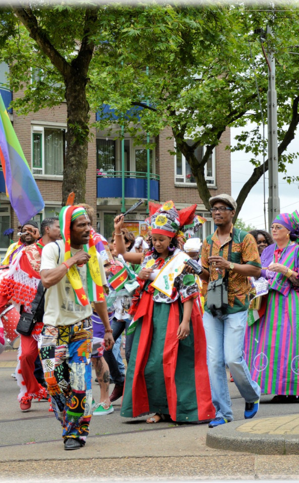 groep mensen loopt door de stad bij herdenking keti koti met vlaggen en in kleurrijke kleding